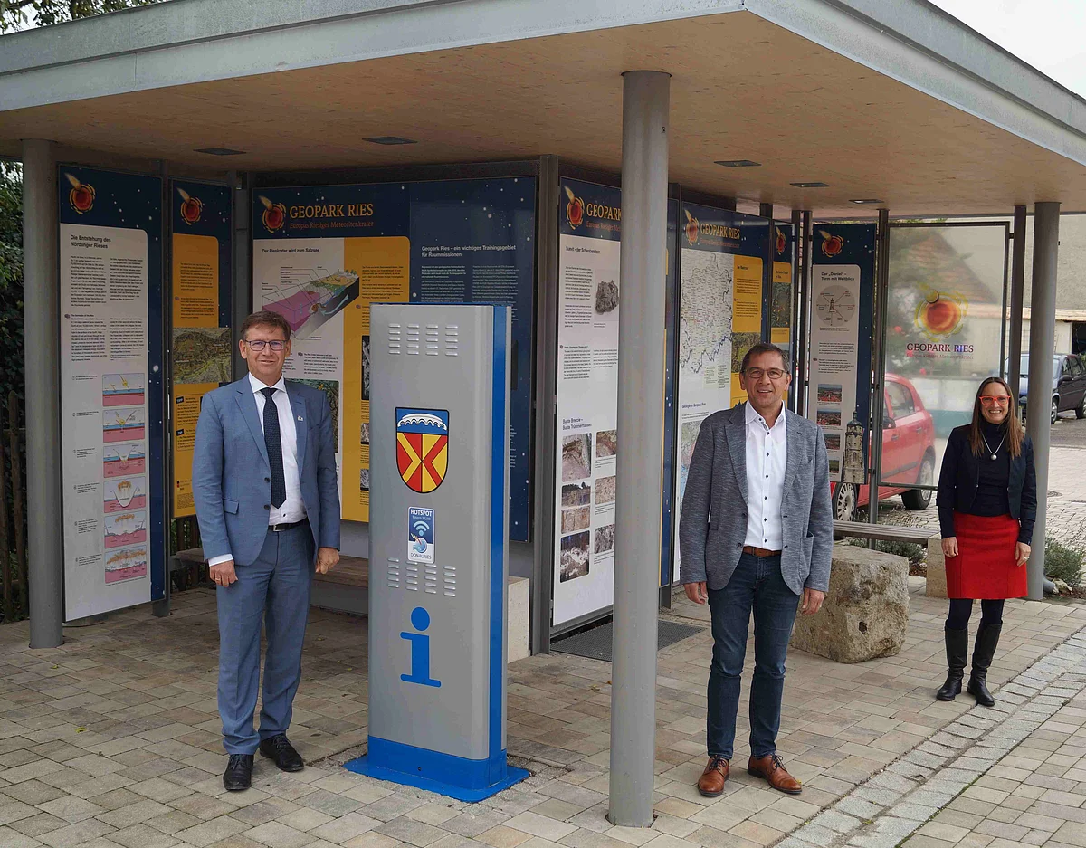 Stefan Rößle und Heike Burkhardt stehen mit dem Bürgermeister Deiningens unter einer Überdachung mit mehreren Informationstafeln zum Geopark Ries.
