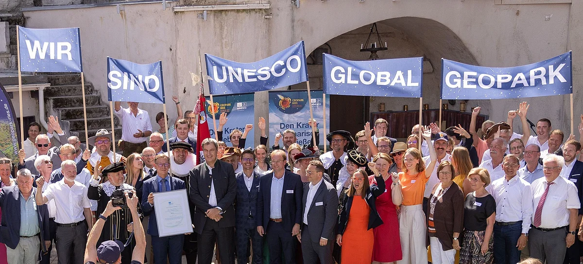 "Wir sind UNESCO Global Geopark" Eine große Gruppe Personen hält Banner mit der Aufschrift "Wir sind UNESCO Global Geopark" in die Höhe.
