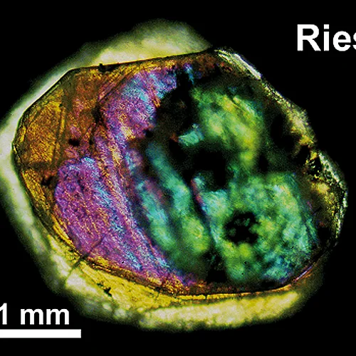Im Dünnschliff schimmert ein etwa 0.3 mm großer Riesdiamat orange, lila und grün.