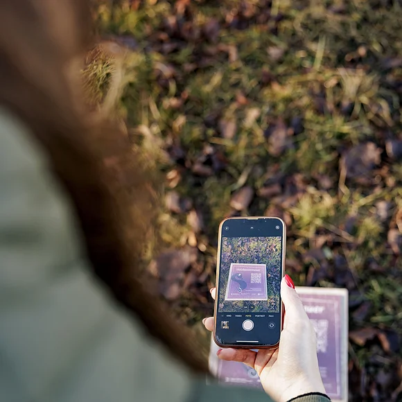 Abscannen eines QR-Codes zum digitalen Rundgang am Ipf Person fotografiert mit Smartphone eine Tafel mit Text und QR-Code auf Grasboden im Freien.